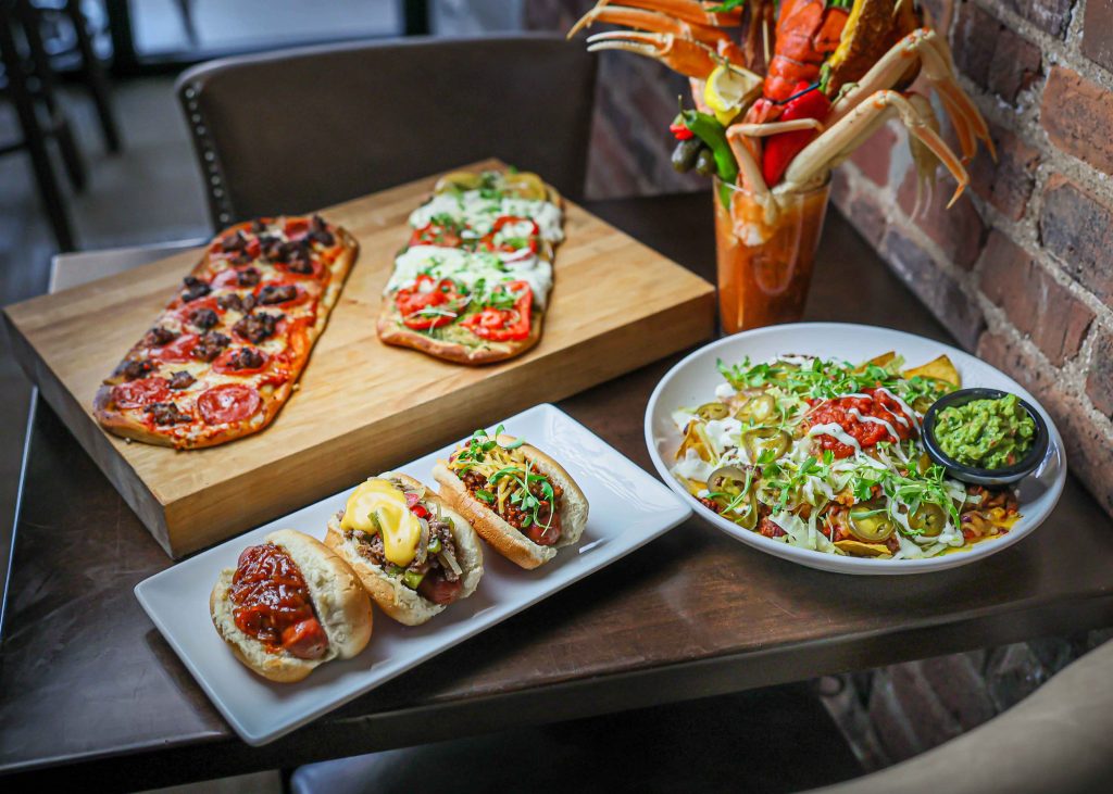 flat bread, mini hotdogs, bloody mary, and big dish of nachos displayed on table